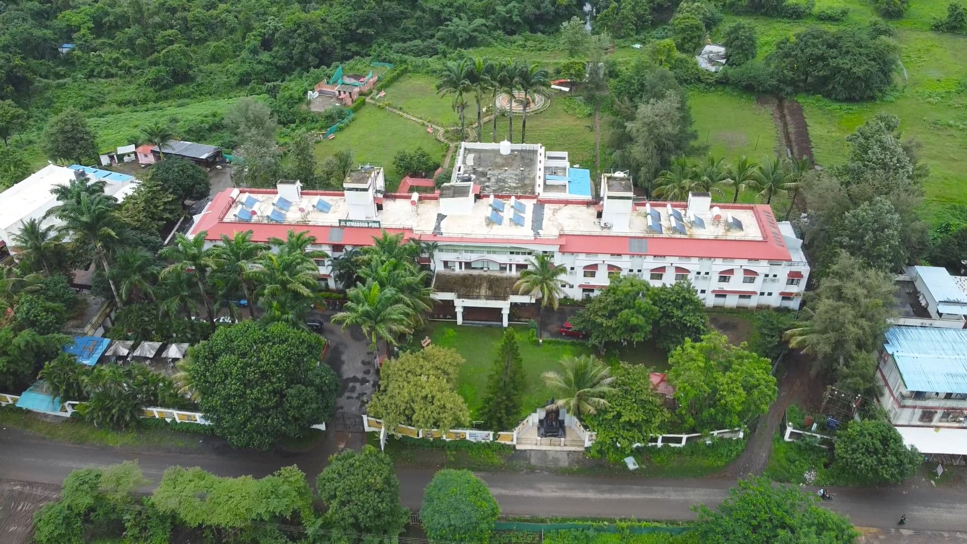 Aerial view of the Atmabodh wellness campus on Sinhagad Road, Pune, surrounded by gardens, palm trees and green hills