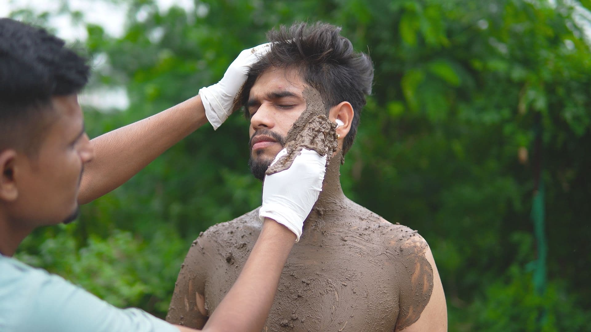 A therapist in gloves applying medicinal mud during a naturopathy mud therapy session outdoors at Atmabodh Wellness Center