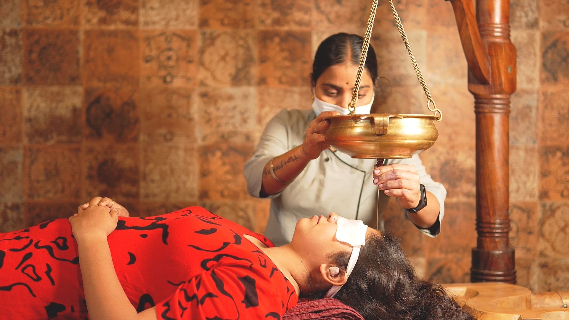 A therapist performing shirodhara, pouring a steady stream of warm oil over a client's forehead, at Atmabodh Wellness Center in Pune
